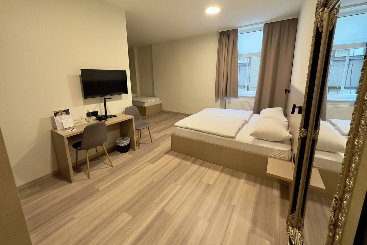 Een hotelkamer met een bed, een bureau, een stoel, een televisie en een raam met gordijnen.