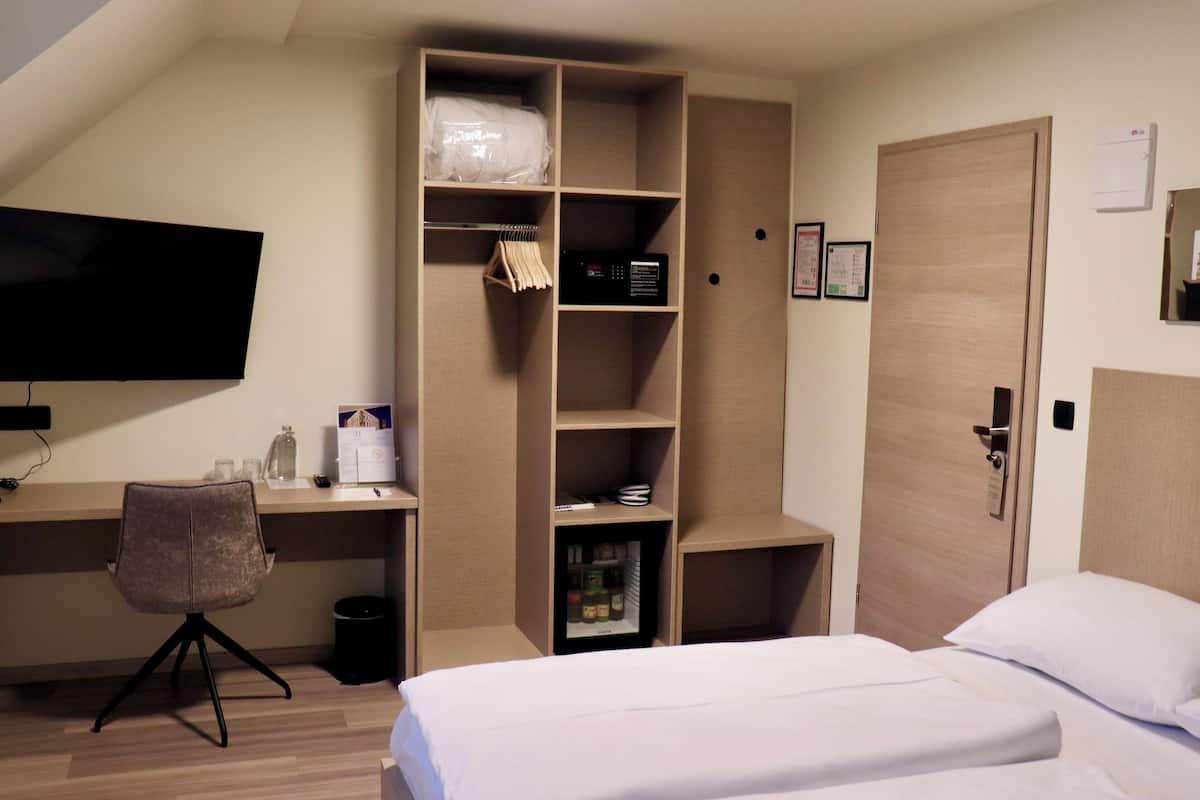 Een hotelkamer met een bed, een bureau met stoel, een televisie, een kledingkast en een deur.