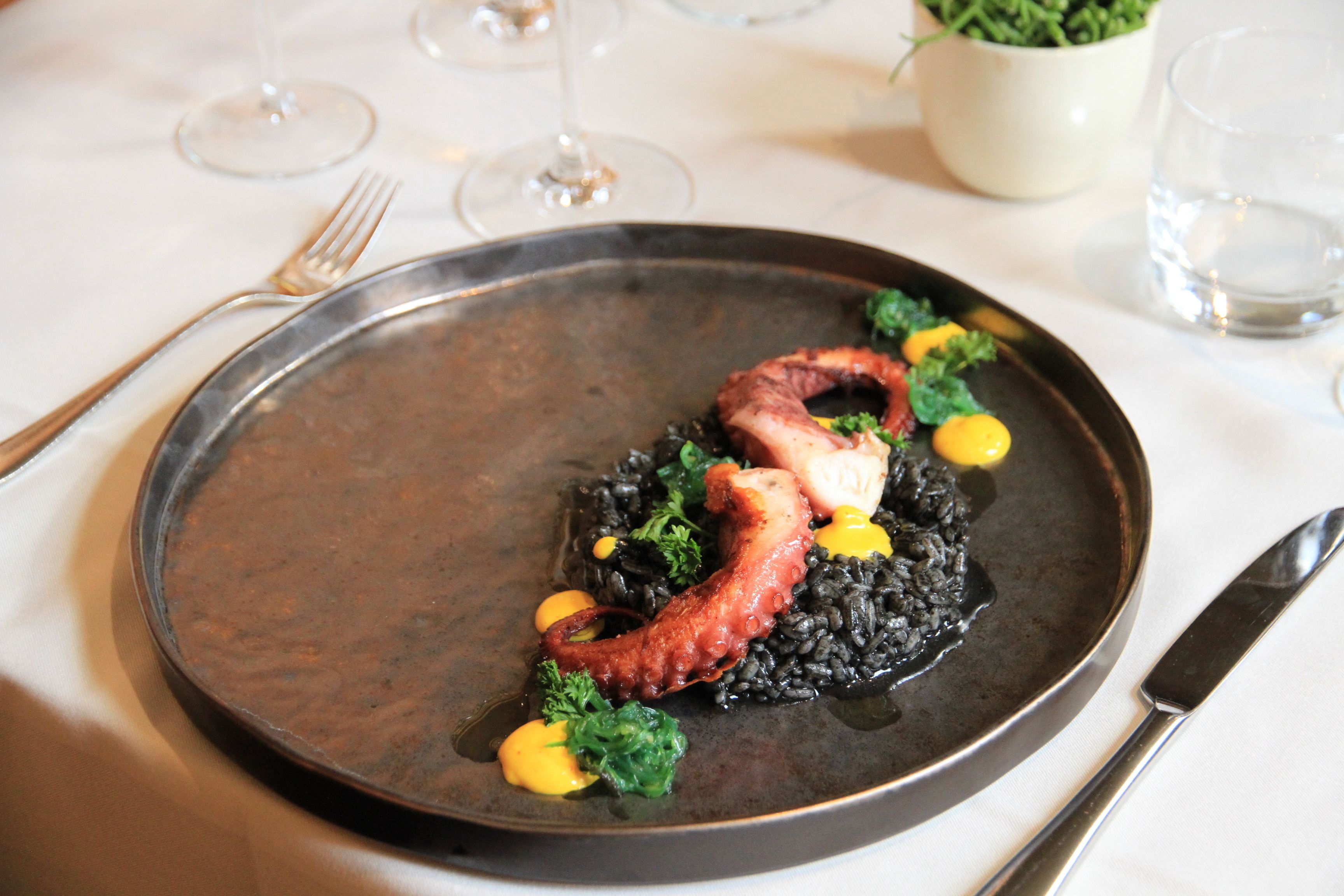 Un plato de risotto negro con calamares y brócoli, servido en un plato oscuro.