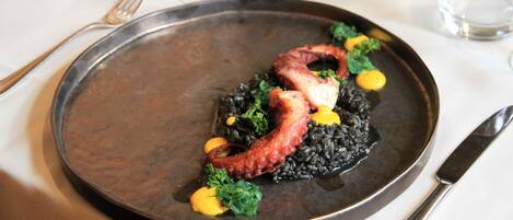 Un plato de risotto negro con calamares y brócoli, servido en un plato oscuro.