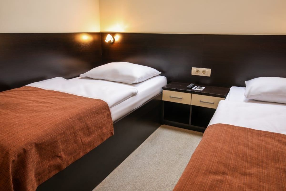 Een hotelkamer met twee eenpersoonsbedden, een nachtkastje met een lamp en een klein dressoir.