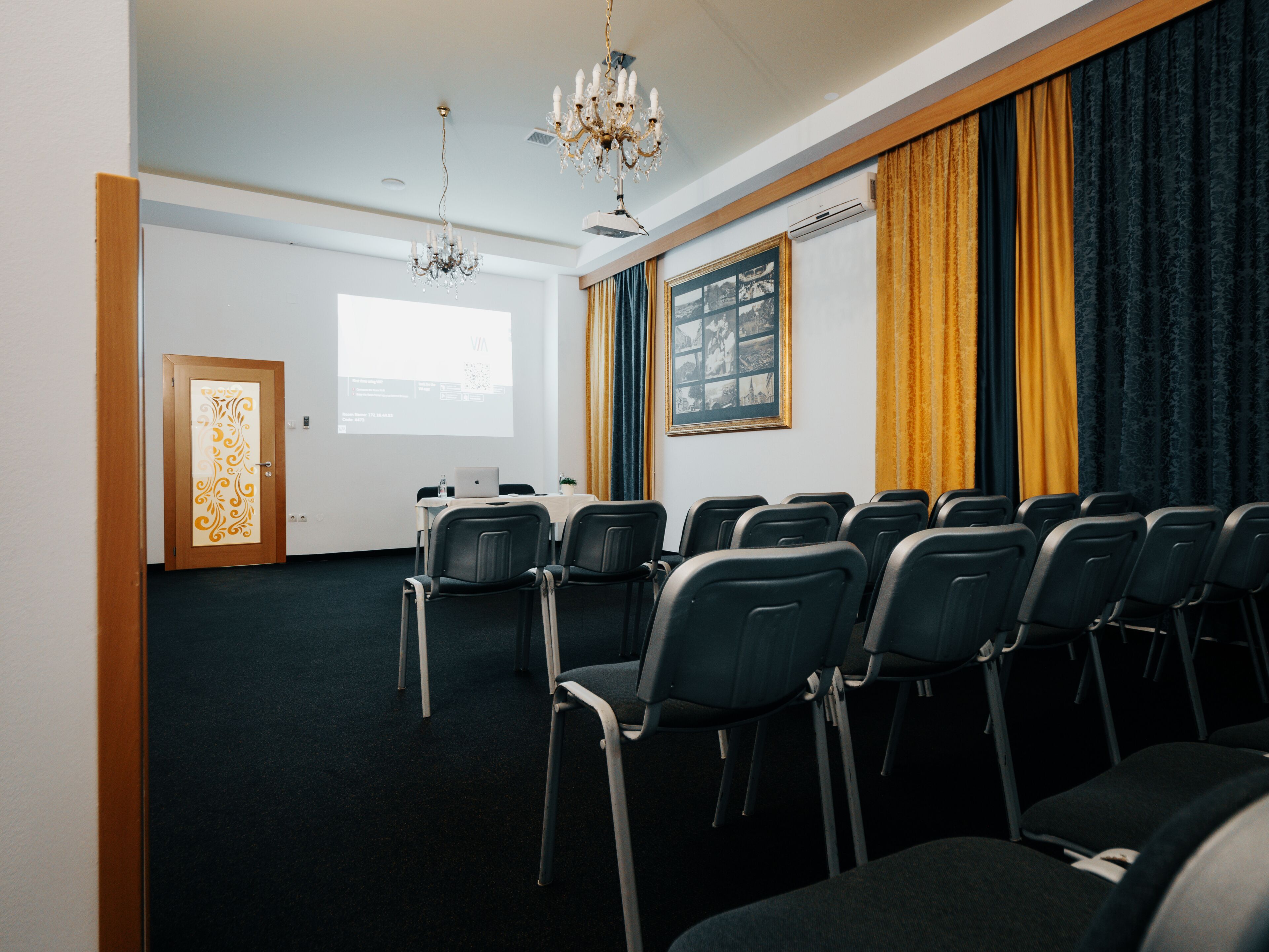A conference room with rows of chairs, a projector screen, and a chandelier.
