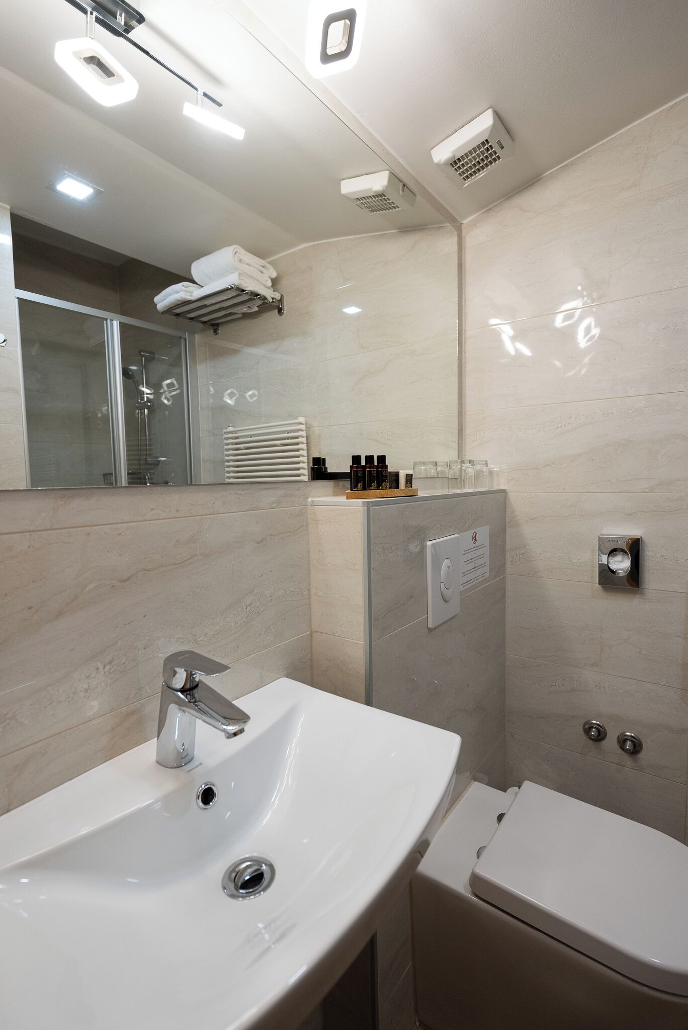 A modern bathroom with a white sink, a toilet, a glass shower enclosure, and a mirror.