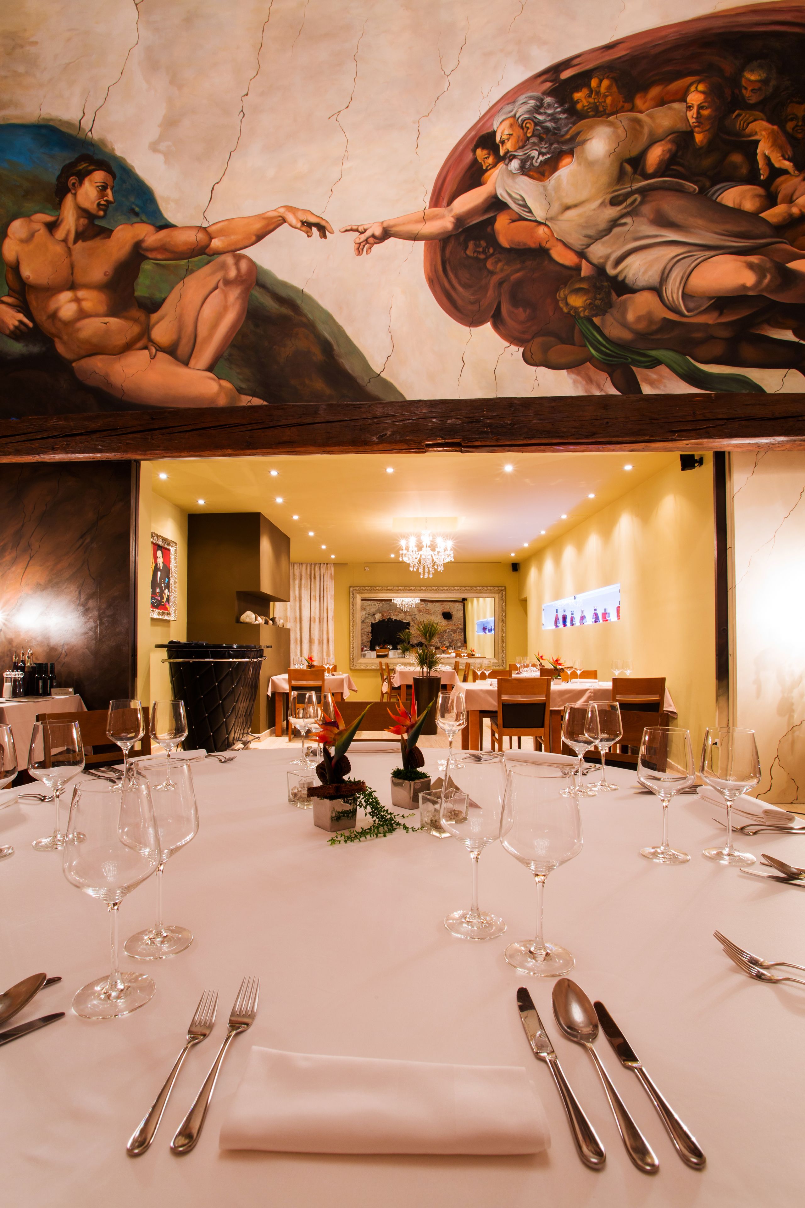A restaurant with a mural, tables set for dining, and a chandelier.