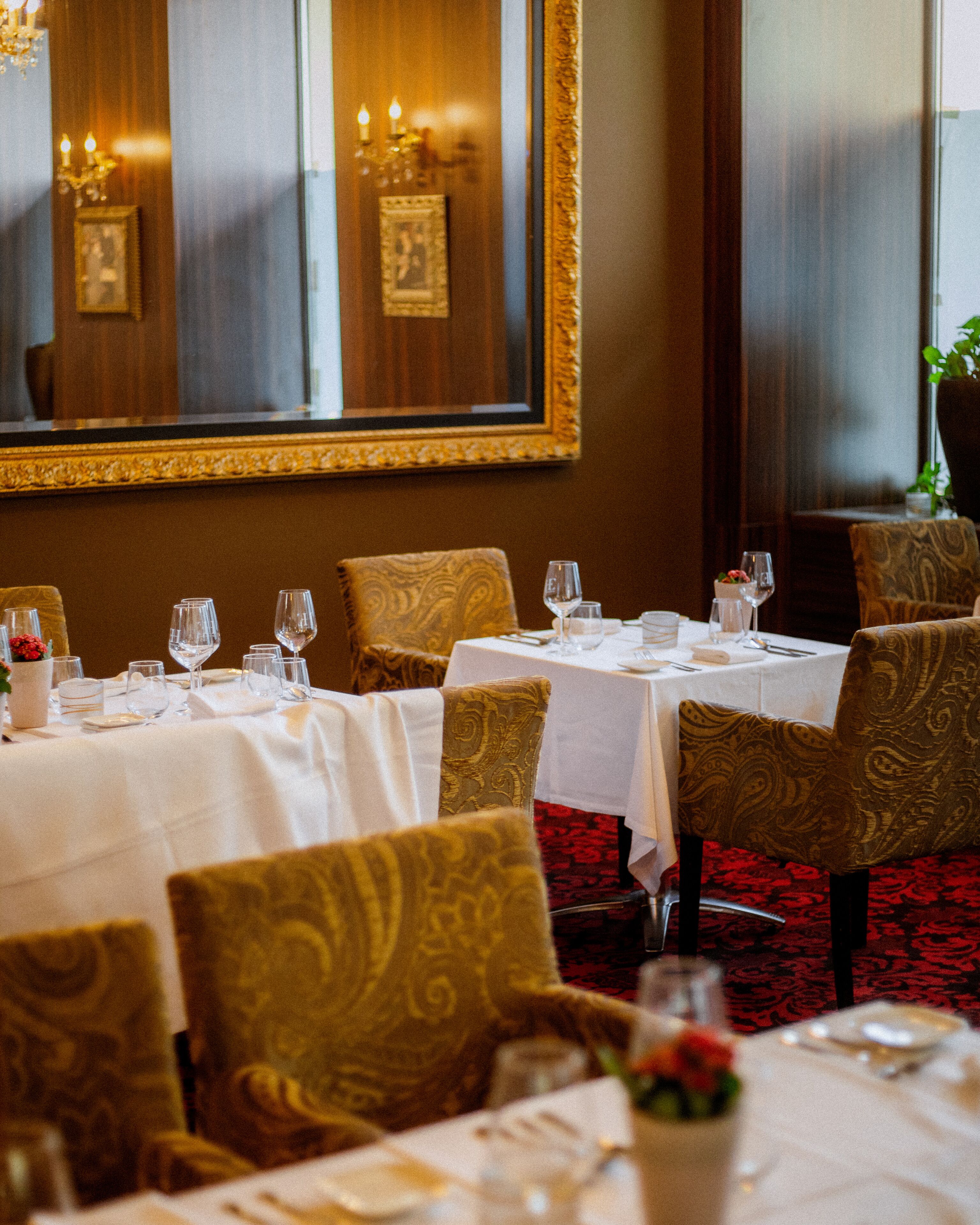 A dining area with tables set for service, chairs with patterned upholstery, and a large mirror on the wall.