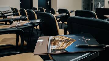 Une salle de conférence avec des rangées de chaises et de tables noires, chacune étant équipée d’une brochure et d’un stylo.