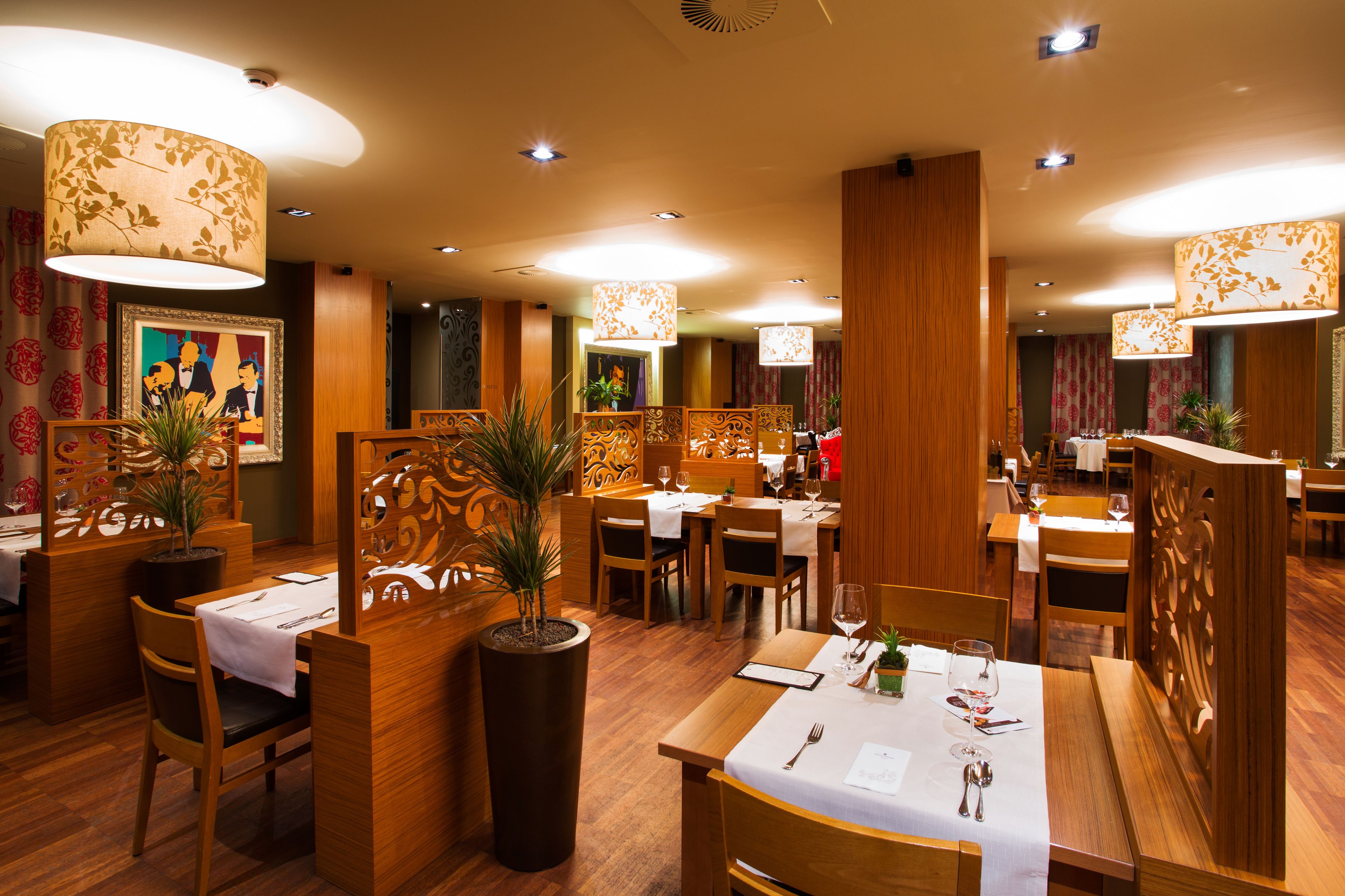 A restaurant with wooden furniture, white tablecloths, and decorative plants.