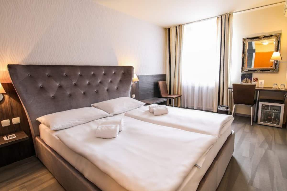 Een hotelkamer met een groot bed, een bureau, een stoel, een spiegel en een raam met gordijnen.