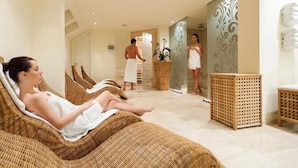 Um espaço de spa com cadeiras reclináveis, mesa de massagem e uma parede com painéis decorativos.