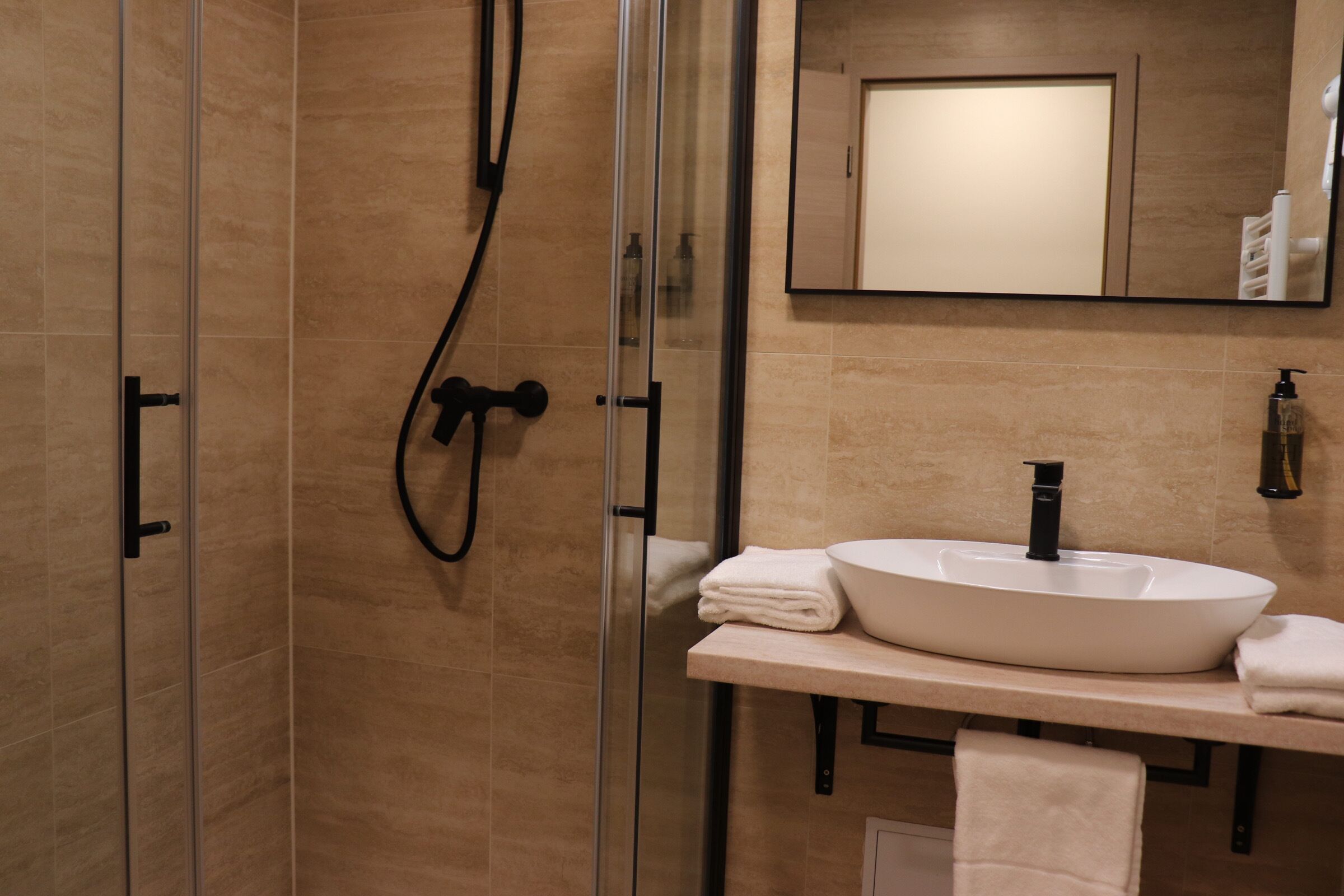 Un baño moderno con ducha de vidrio, lavamanos blanco y espejo sobre el lavamanos.