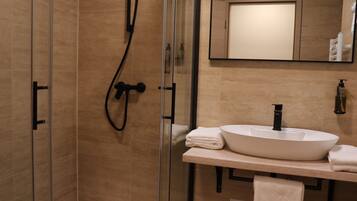 Un baño moderno con ducha de vidrio, lavamanos blanco y espejo sobre el lavamanos.