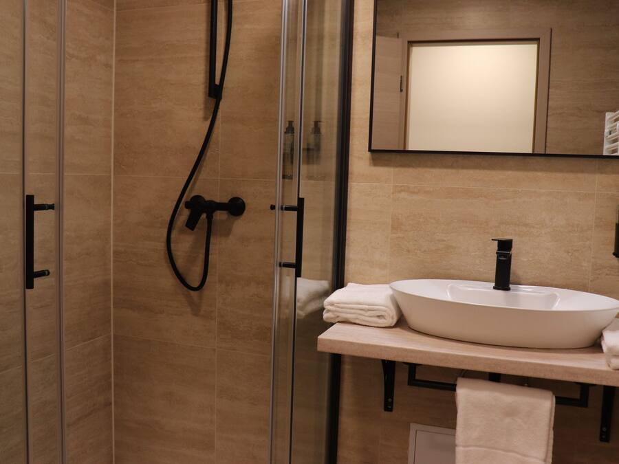 Un baño moderno con ducha de vidrio, lavamanos blanco y espejo sobre el lavamanos.