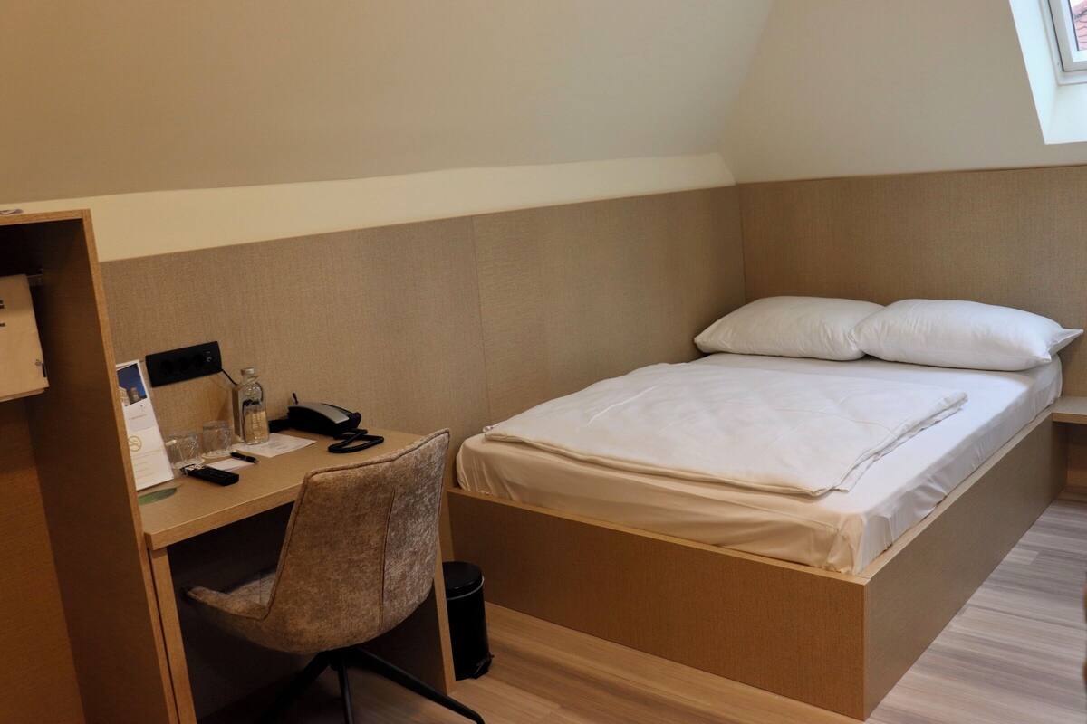 Een kleine slaapkamer met een bed, bureau en stoel.
