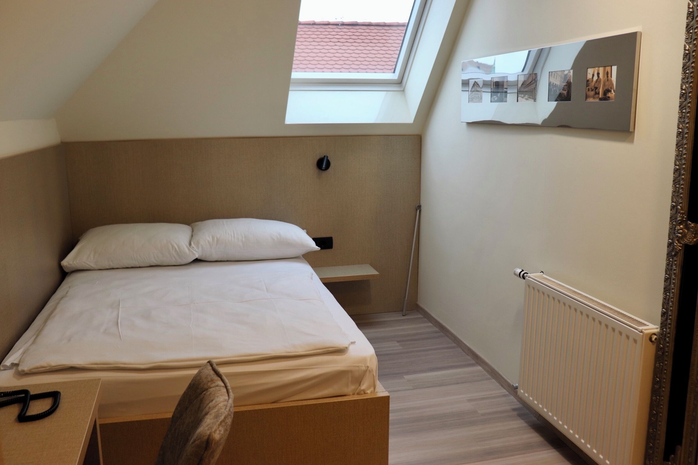 A bedroom with a bed, a nightstand, a mirror, a radiator, and a skylight.