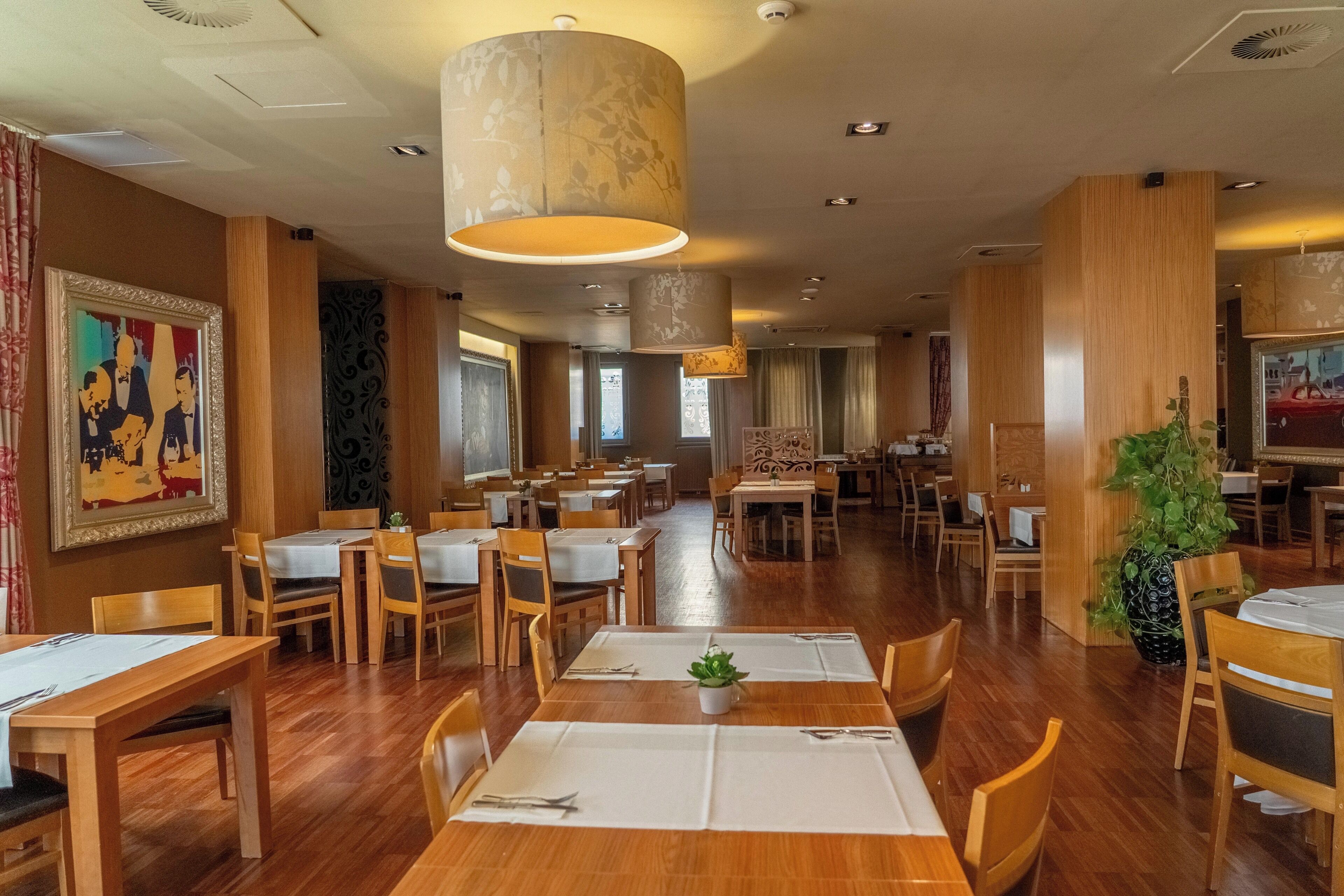 Un restaurante con mesas y sillas de madera, un candelabro colgante grande y una planta en maceta.