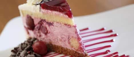 Ein Stück mehrschichtiger Dessert mit einer Kirsche oben, serviert auf einem weißen Teller mit roter Glasur.
