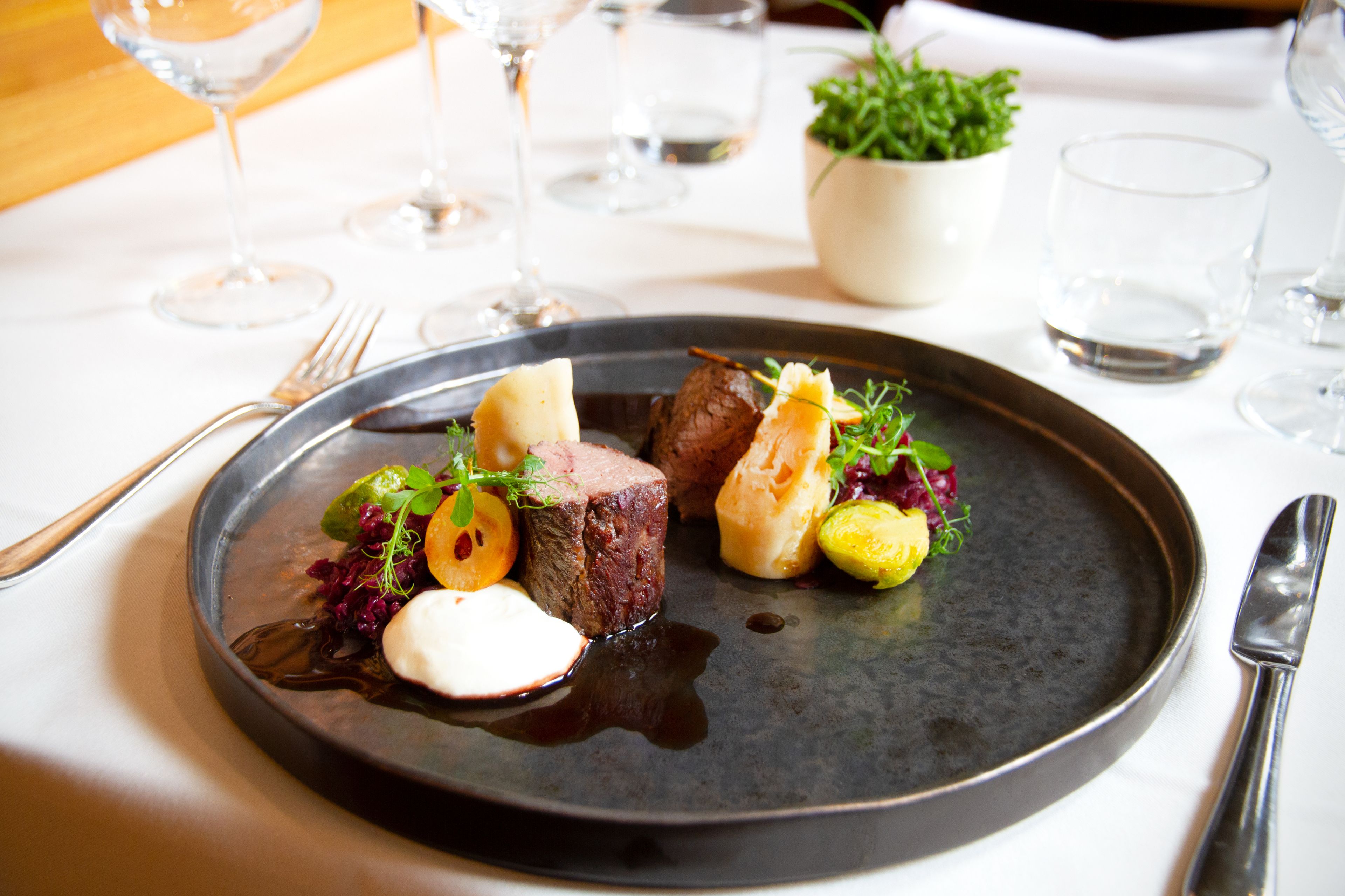 A plate of food with a dark plate, a fork, and a knife on the table.