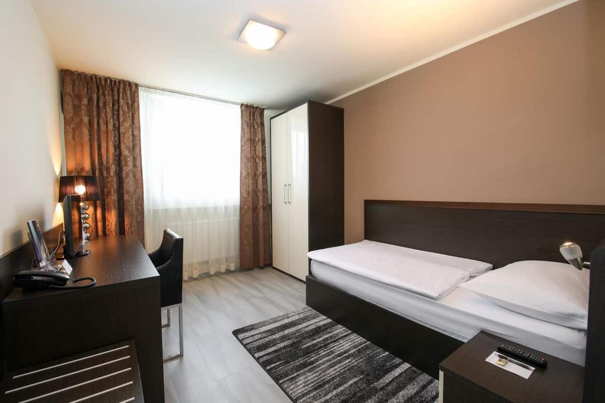 Een hotelkamer met een bed, een bureau, een stoel, een bureaulamp, een telefoon en een raam met gordijnen.