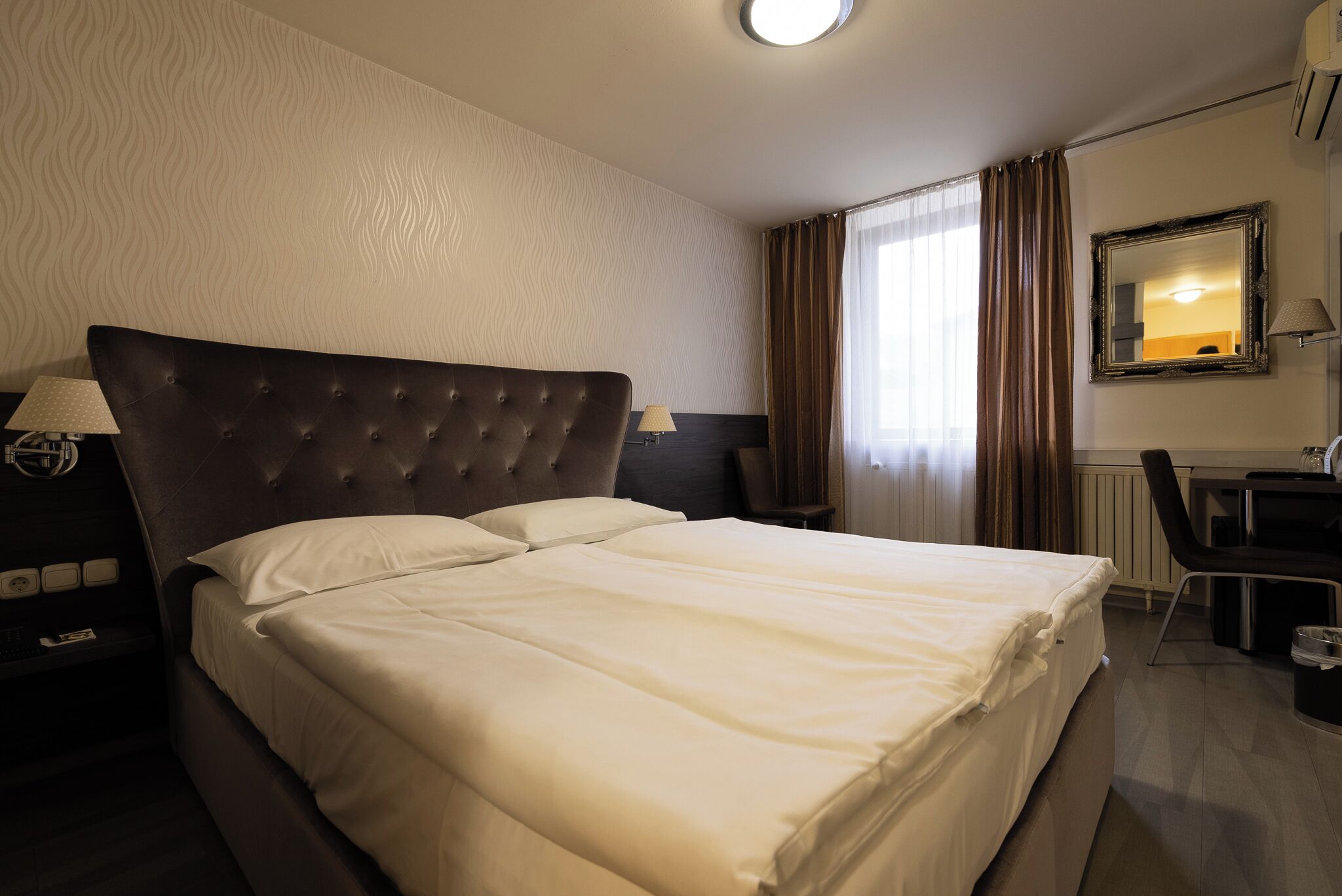A hotel room with a large bed, two bedside tables with lamps, a desk, and a chair.