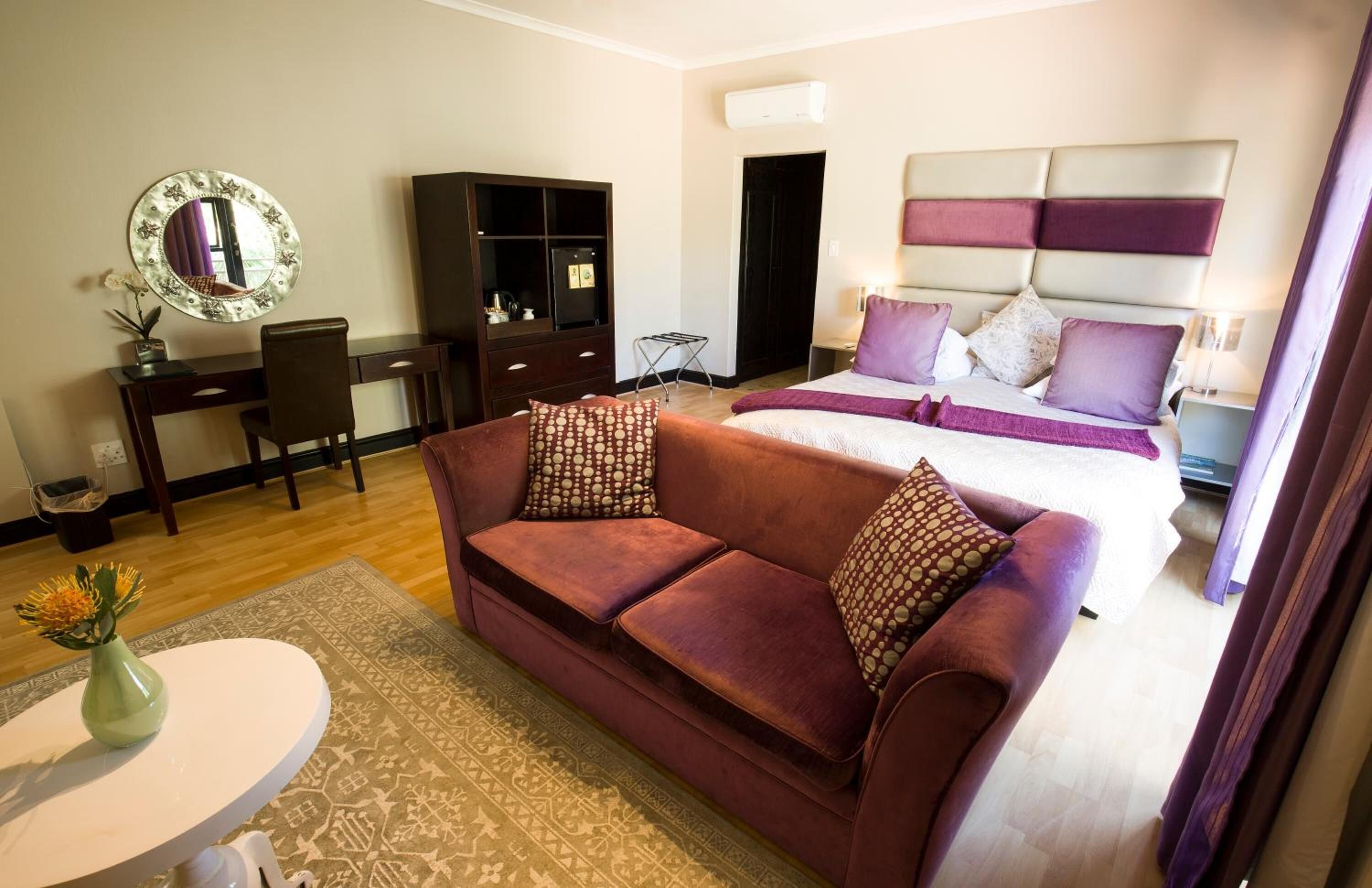 Quarto de hotel com cama, sofá, escrivaninha, espelho e guarda-roupa.