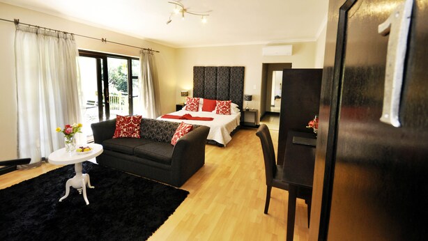 A modern hotel room with a bed, a sofa, a small table with a vase of flowers, and a desk. - Southern Light Country House (Cape Town)