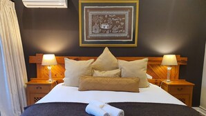A neatly made bed with a rolled towel, two bedside lamps, and a framed picture on the wall.