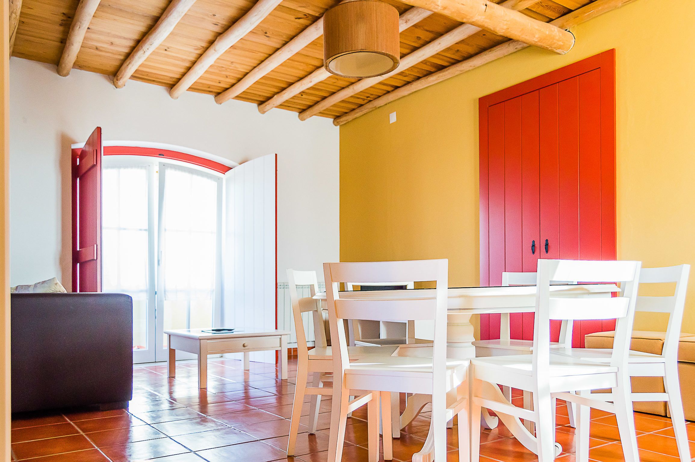Un coin repas avec une table et des chaises blanches, une porte rouge et un plafond en bois.
