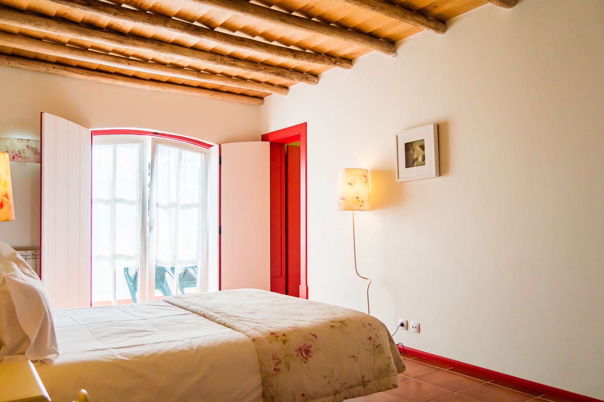 Un dormitori amb un llit, una porta vermella, una làmpada penjada a la paret i una pintura a la paret.