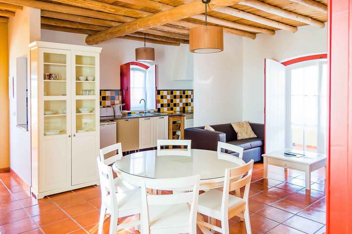 Una cocina compacta con una mesa y sillas, un armario empotrado y un ventanal con marco rojo.