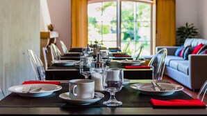 A dining table set with plates, glasses, and cutlery, with a view of a living room and a window in the background. - Casa da Padeira - TER (Alcobaça)