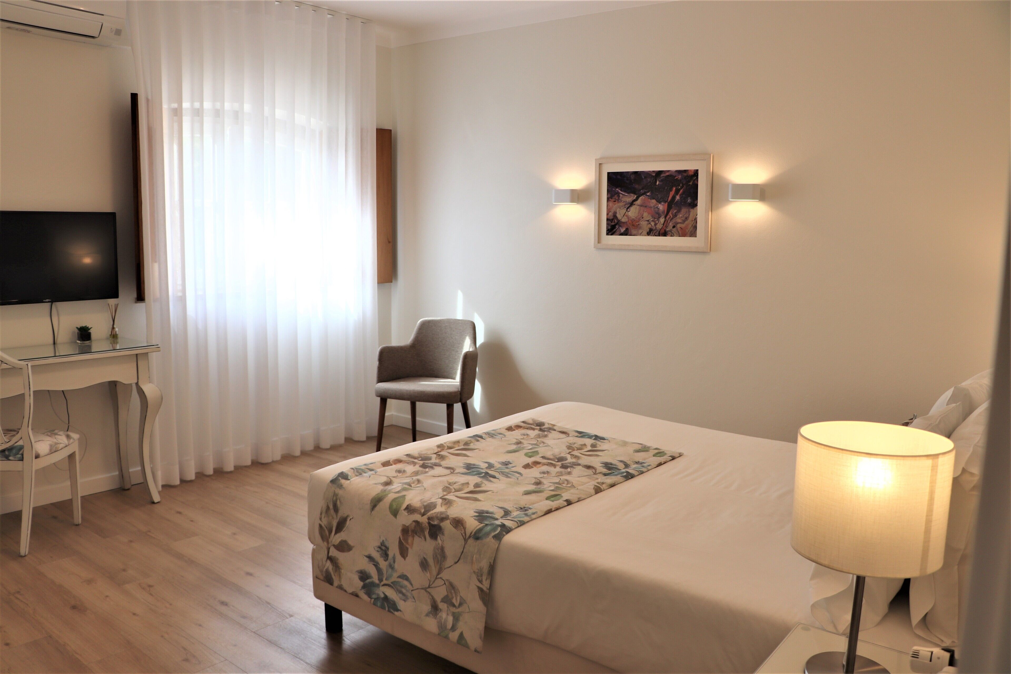 Habitación de hotel con cama, escritorio, silla, televisor y un cuadro en la pared.