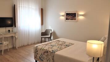 Habitación de hotel con cama, escritorio, silla, televisor y un cuadro en la pared.