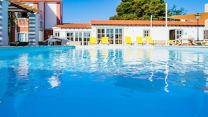 A swimming pool with clear blue water, yellow lounge chairs, and a building with a red-tiled roof in the background. - Casa da Padeira - TER (Alcobaça)