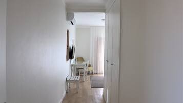 A hallway with a white bench, a table with chairs, and a TV mounted on the wall.