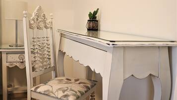 A white, ornate chair with a cushioned seat and backrest, positioned next to a white table with a glass top.
