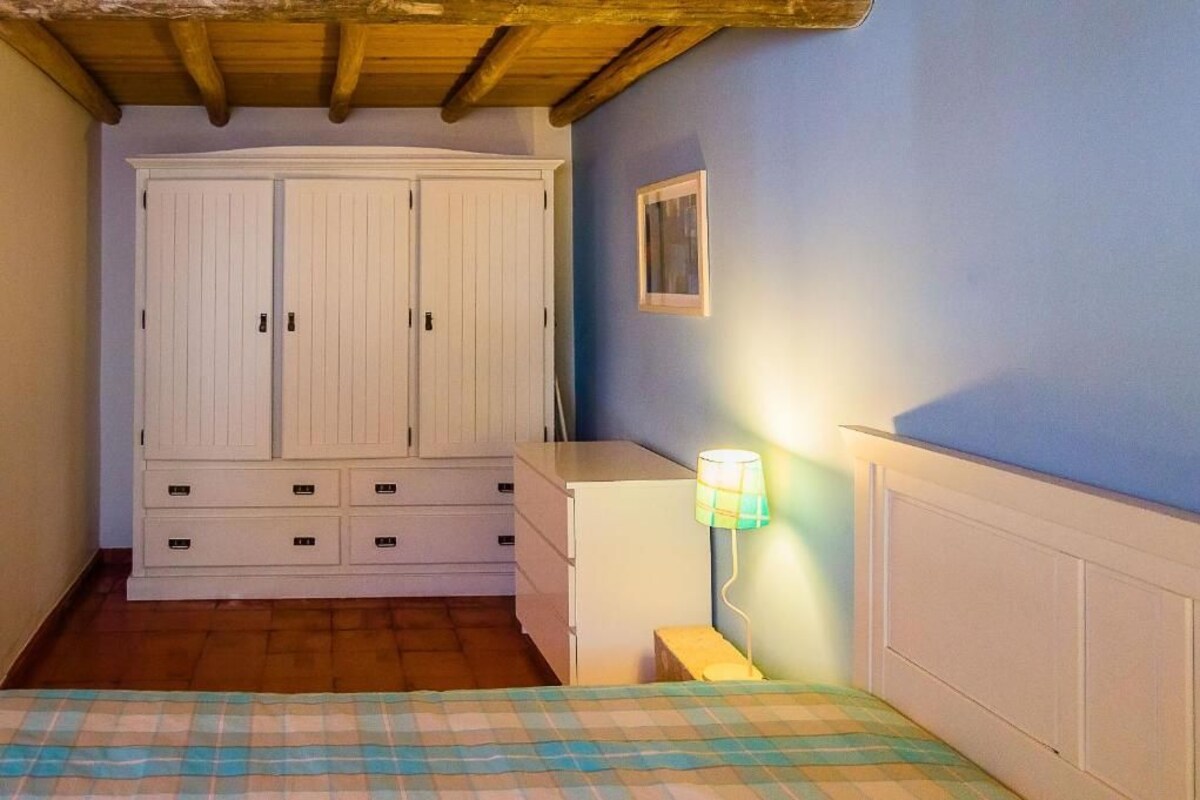 A bedroom with a bed, a wardrobe, a bedside table, and a lamp.