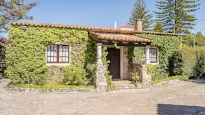 A stone building with a tiled roof, covered in green ivy, and a wooden door. - Casa da Padeira - TER (Alcobaça)