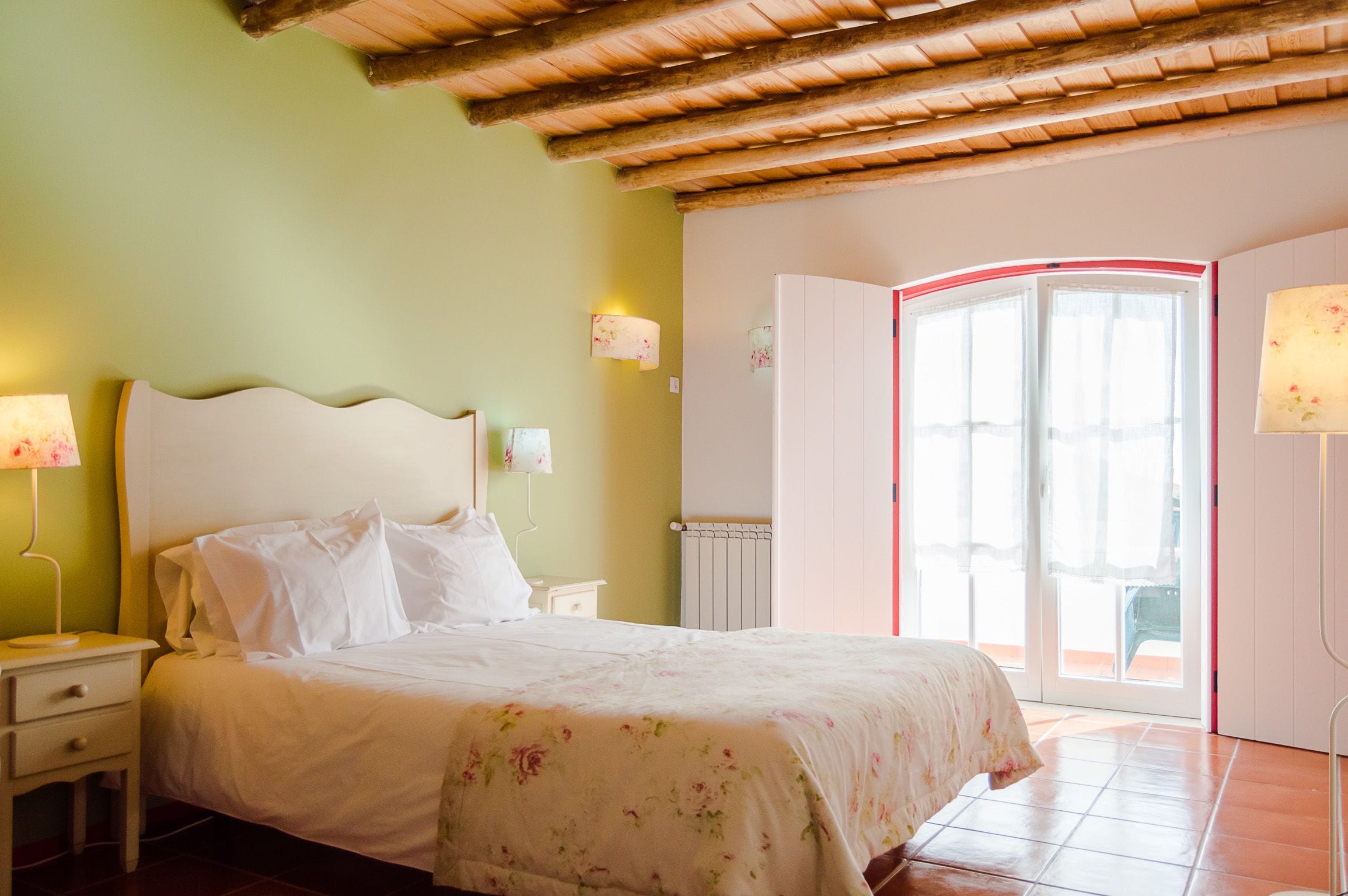 Een slaapkamer met een bed, nachtkastjes, een lamp, een radiator en een deur die leidt naar een buitenruimte.