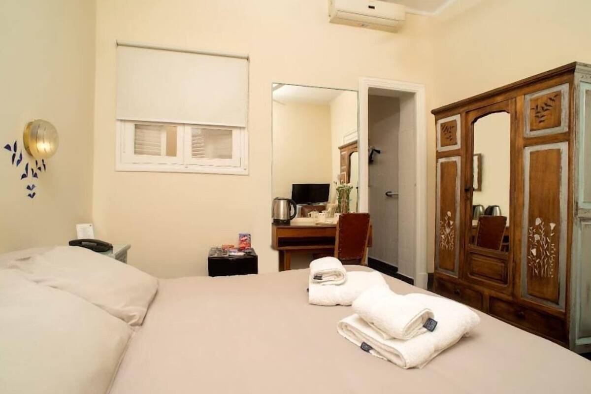 Habitación de hotel con cama, escritorio, espejo, armario y ventana con persianas.