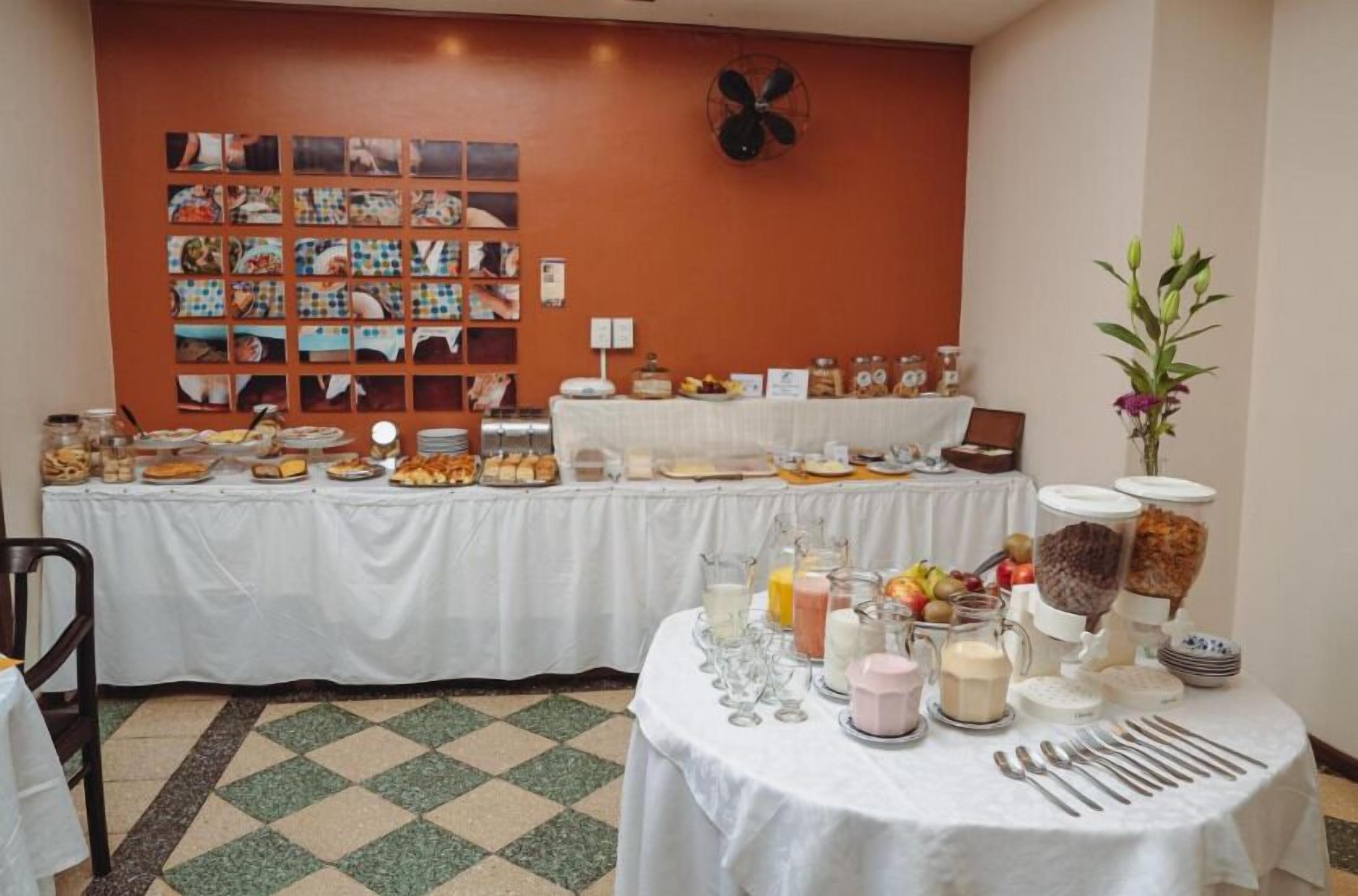A breakfast buffet with various food items and beverages, a wall with photos, and a fan on the ceiling.