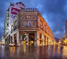 Un edificio histórico de estilo colonial, con una entrada destacada y varias tiendas a nivel de calle.