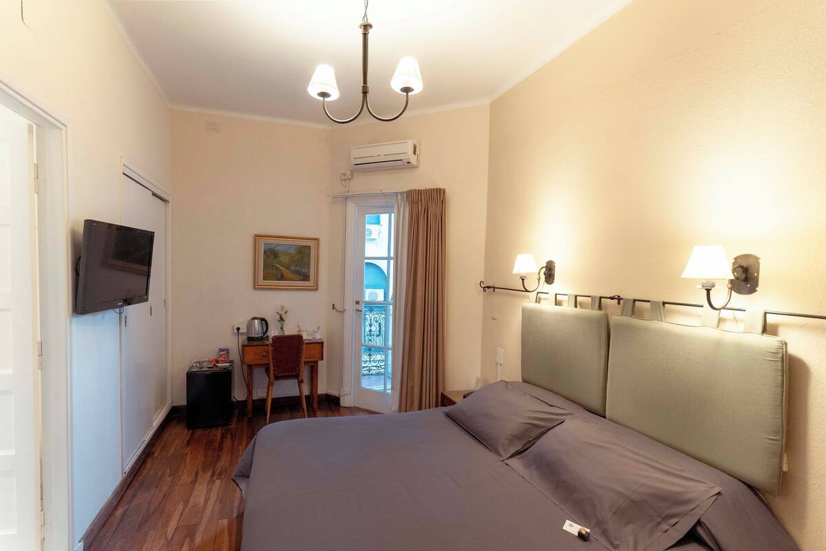 Una habitación de hotel con una cama, un escritorio con silla, un televisor y una ventana con cortinas.