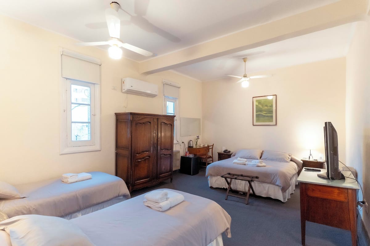 Habitación de hotel con dos camas, un armario de madera, un escritorio con una computadora y ventiladores de techo.