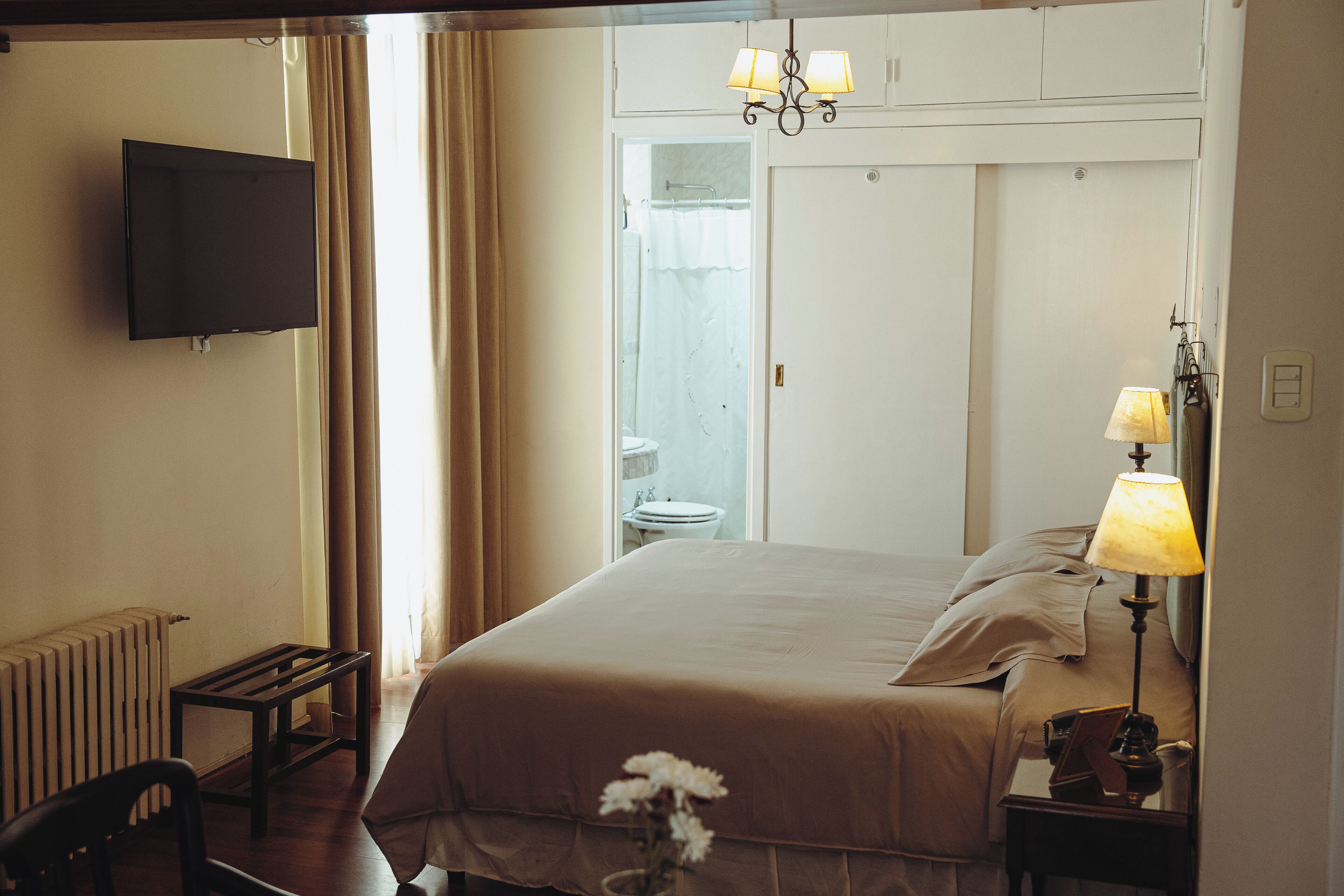 A hotel room with a bed, bedside lamps, a TV, a small table, and a chair.