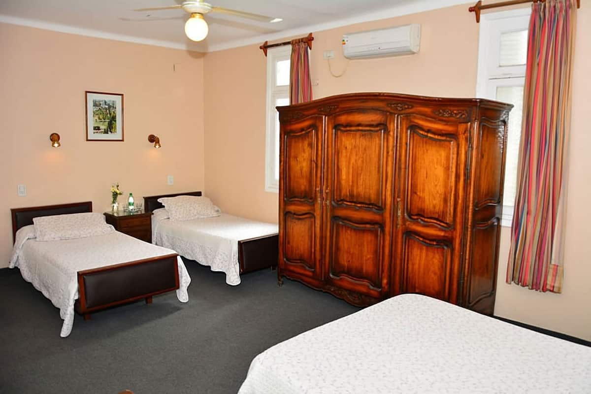 Habitación de hotel con dos camas individuales, un armario de madera, un equipo de aire acondicionado y un ventilador de techo.