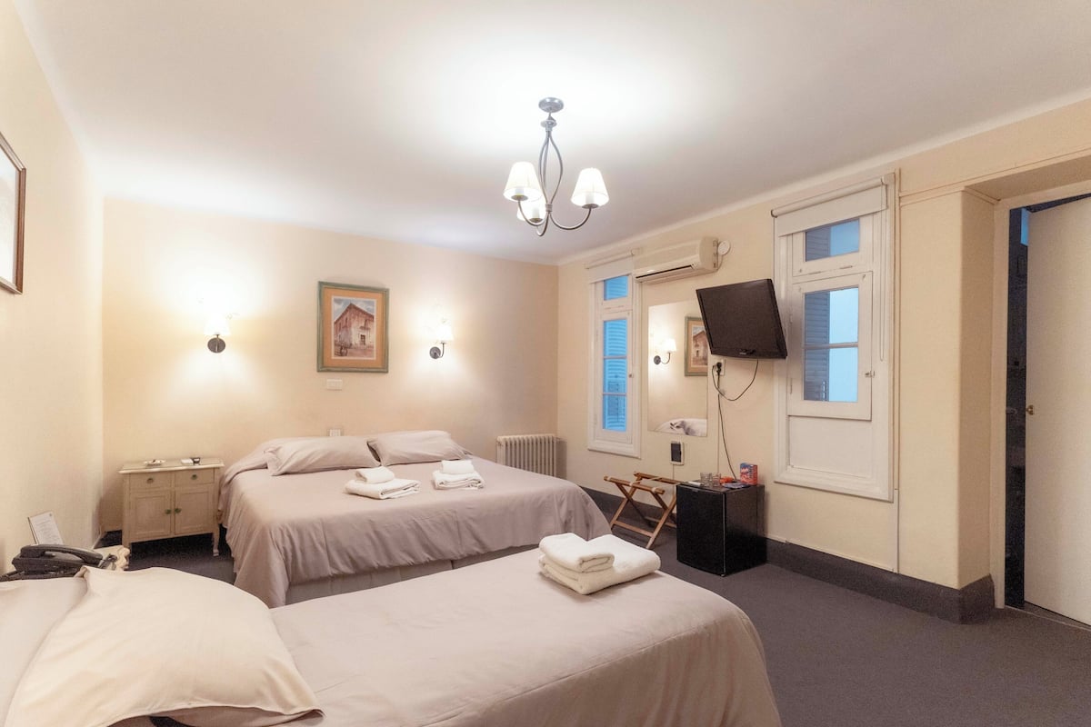 Una habitación de hotel con dos camas, un escritorio, una silla, un televisor y una ventana.