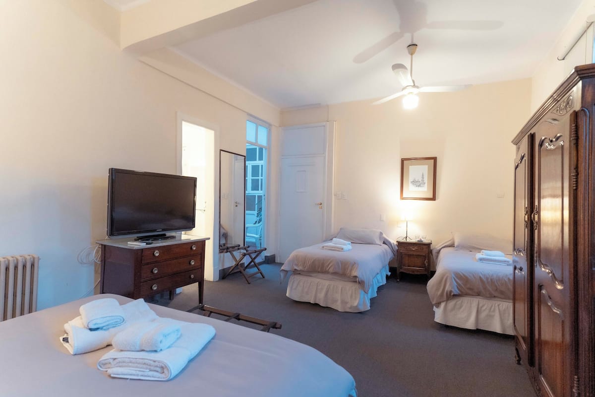 Una habitación de hotel con televisión, dos camas, un armario y un ventilador de techo.
