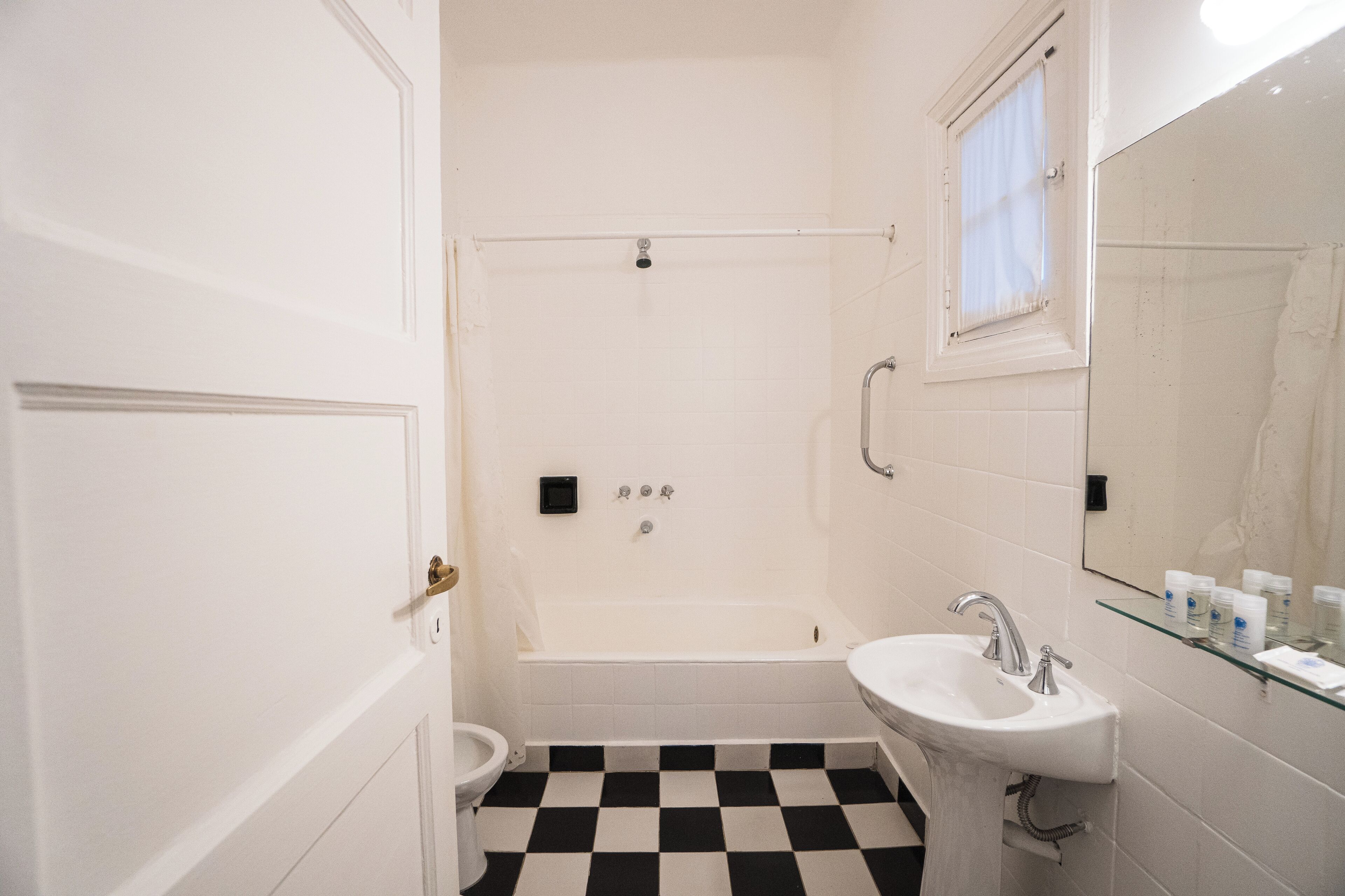 A bathroom with a bathtub, a sink, a toilet, and a glass shelf with toiletries.