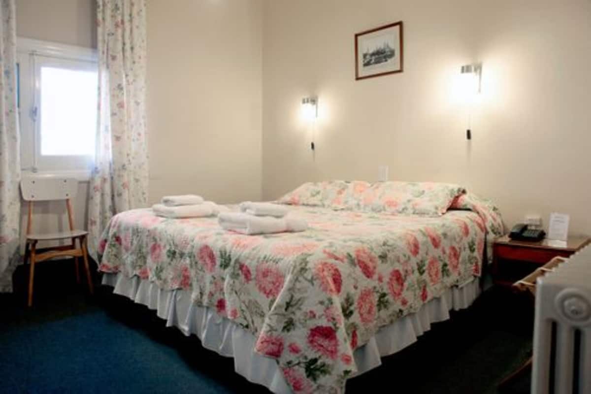 Una habitación con cama, una silla, una mesita de noche y una lámpara fijada a la pared.