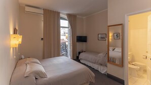 A hotel room with two beds, a TV, a mirror, and a bathroom.
